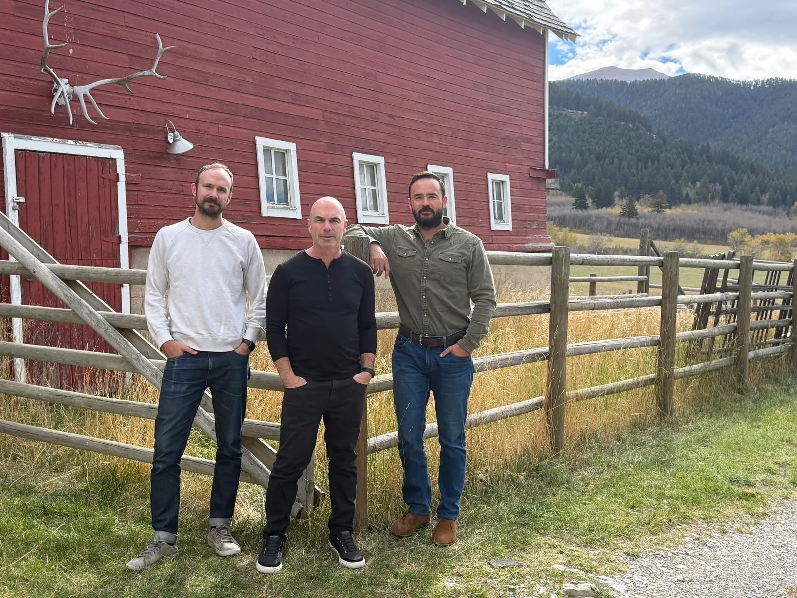 Nathanael Wolfe, Issac Roth and Casey Clark, Elk’s founders, standing by a red barn and a rail fence with forested mountains behind them.